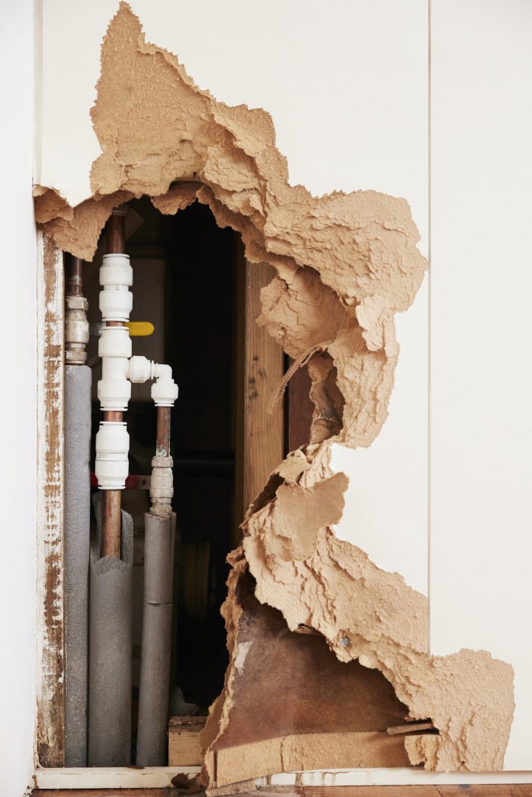 Damaged wall exposing burst water pipes after flood, vertical